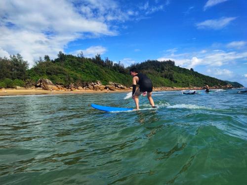 a man standing on a surfboard in the water at Wan Ning Xiao Gang Guest House in Wanning