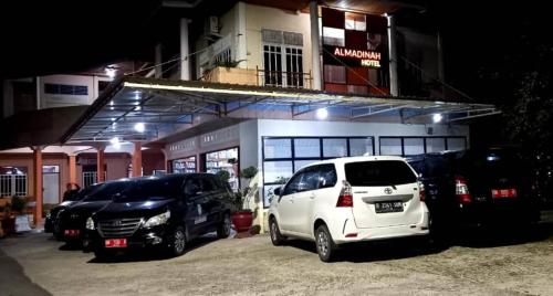 Hotel Al Madinah Bangkinang في Bangkinang: سيارتين متوقفتين في موقف للسيارات امام مبنى