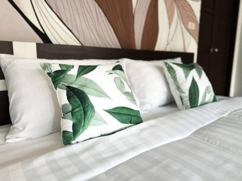 Una cama con almohadas blancas con hojas verdes. en SID house en Ban Hua Laem Ma So