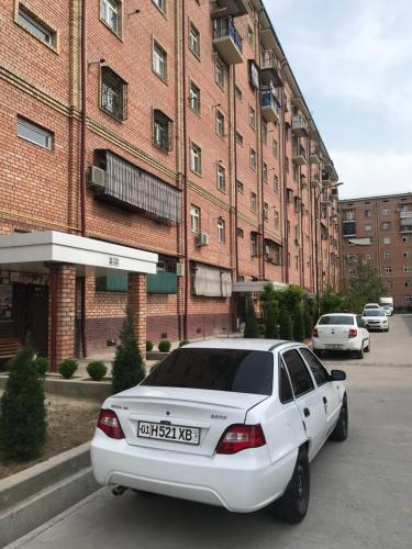 ein weißes Auto, das vor einem Backsteingebäude parkt in der Unterkunft Sergeli 9 Resedens in Taschkent