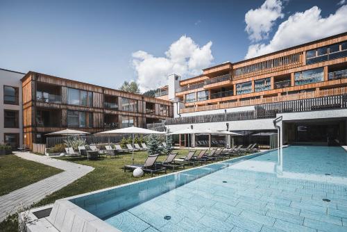 a hotel with a swimming pool and chairs and a building at Hirben Naturlaub in Villabassa