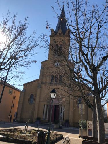 a church with a tall tower with a tree at Le Nid du bois d'Oingt in Le Bois-dʼOingt