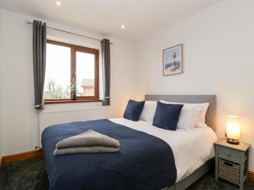 a bedroom with a bed with a blue blanket and a window at Bluebell Lodge, Meadow view lodges in Burnham on Sea