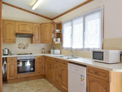 a kitchen with wooden cabinets and a sink and a microwave at Merlins Cabin in Cenarth