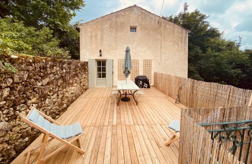 a wooden deck with chairs and an umbrella and a building at Clos Labellie - Gîte et Chambre d'Hôtes à Saint-Emilion in Lugaignac