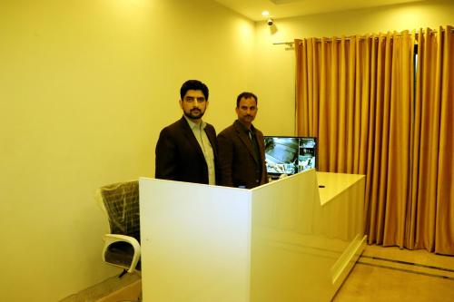 Dois homens atrás de um balcão com um computador. em Hayat Grand Guest House em Islamabad