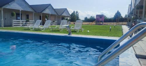 a swimming pool with white chairs and a table at Domki Biel i Zieleń in Nacmierz