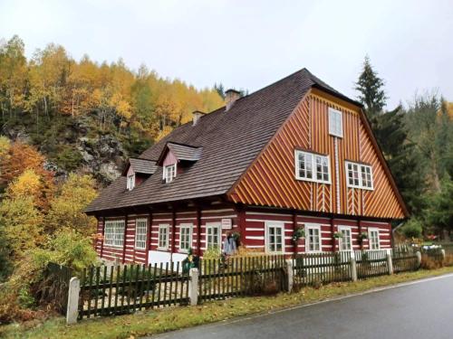 a red house with a black roof and a fence at Roubenka Mlýn u skály Deštné v Orlických horách volné termíny 5 bytů in Deštné v Orlických horách