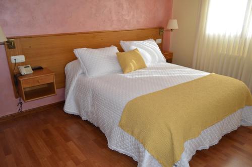 a bedroom with a large bed with a yellow and white blanket at Hotel Restaurante Val in Antas de Ulla