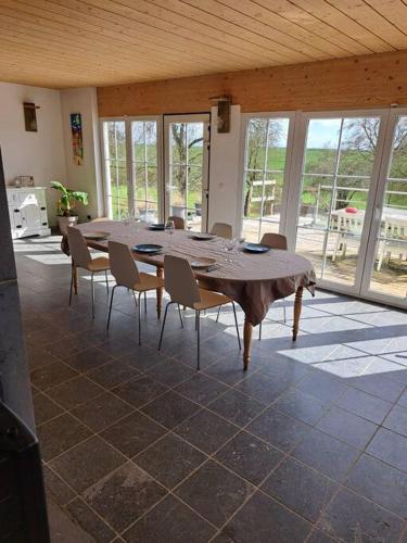a large table and chairs in a room with windows at Le Floyon (avec piscine) in Florennes