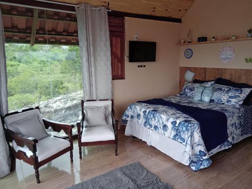 a bedroom with a bed and two chairs and a window at Chalé Mirante da Pedra in Serra de São Bento
