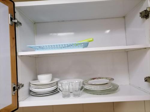 a white cabinet with plates and cups and dishes at MBZ - Comfortable Room in Unique Flat in Abu Dhabi