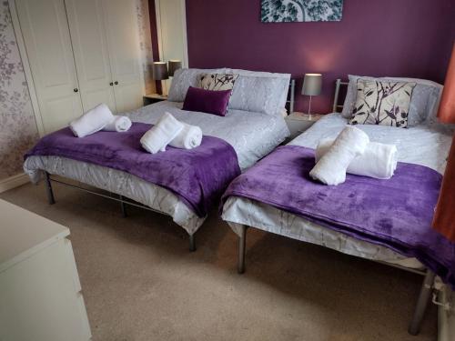 two beds in a room with purple sheets and pillows at Edelweiss House in Great Barr