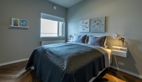 een slaapkamer met een bed met een blauw dekbed en een raam bij Iceland SJF Apartments - 503 in Reykjavík