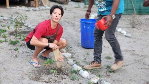 a young man planting a tree in the sand at Beyond Brahmaputra Campsite in Brahmakund