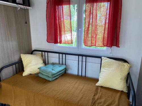 ein Bett mit zwei Kissen und ein Fenster mit roten Vorhängen in der Unterkunft Bungalow climatisé dans un bel écrin de nature in Saint-Chéron
