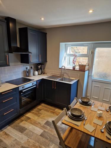eine Küche mit schwarzen Schränken und einem Holztisch in der Unterkunft Lovely Cosy Two Bed Home,Peak District Gateway in Buxton
