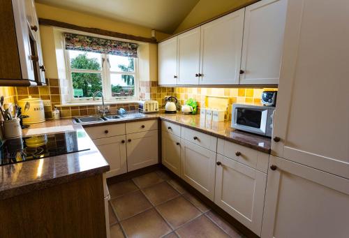a kitchen with white cabinets and a microwave at Hollyhock Cottage, Clematis cottages, Stamford in Stamford