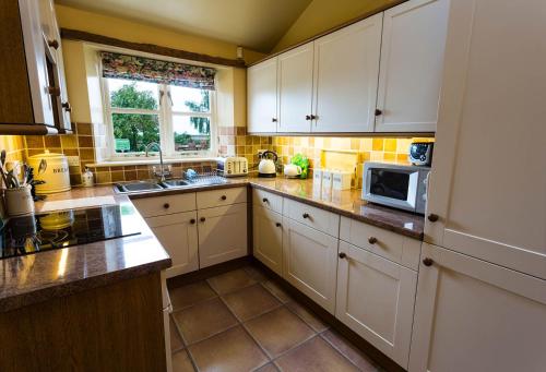 una cucina con mobili bianchi e un forno a microonde di Hollyhock Cottage, Clematis cottages, Stamford a Stamford