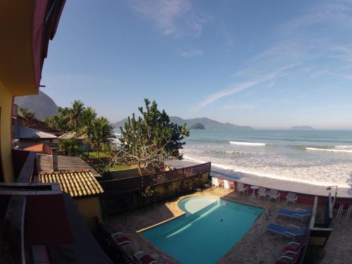 a swimming pool next to a beach with chairs and the ocean at Pousada Casa na Praia in Ubatuba