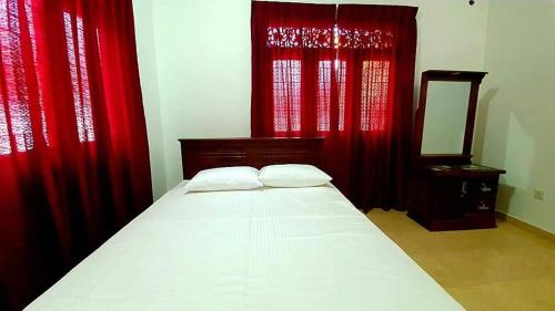 a bedroom with a bed with red curtains and a mirror at Villa 87 in Katunayake