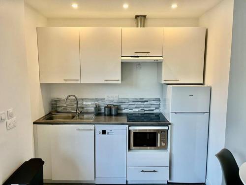 une cuisine avec des armoires blanches, un évier et un réfrigérateur dans l'établissement Le triangle d'or Paris-CDG- Disney, à Vaires-sur-Marne