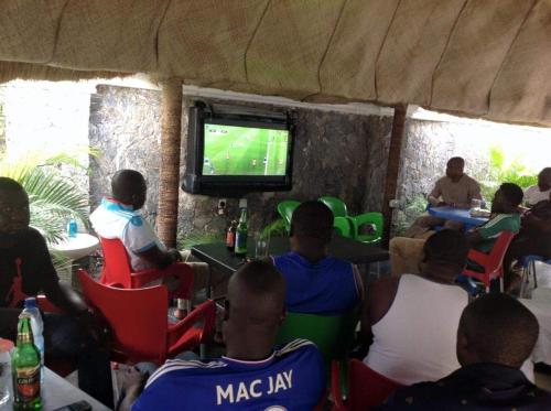 grupa ludzi siedzących w fotelach oglądających mecz piłki nożnej w obiekcie Blue-View Suites & Apartments w mieście Abudża