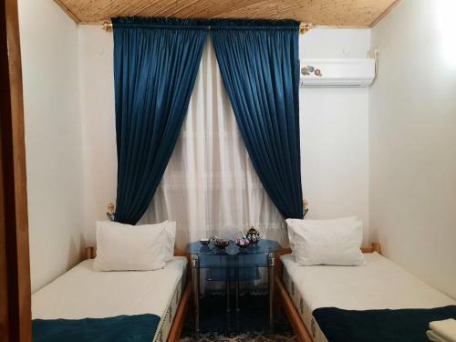 two beds in a room with a window with blue curtains at Boutique Hotel Parvina in Bukhara