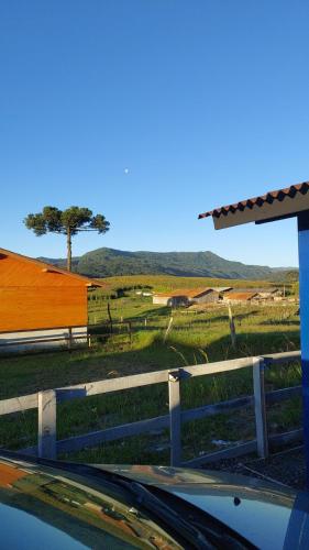 a fence in front of a field with a tree at Cabana Brisa Do Valle in Urubici