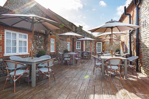 an outdoor deck with tables and chairs and umbrellas at The Manor Coastal Hotel & Inn, Blakeney - The Coaching Inn Group in Blakeney