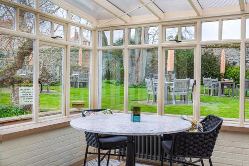 a conservatory with a table and chairs in a room with windows at The Manor Coastal Hotel & Inn, Blakeney - The Coaching Inn Group in Blakeney