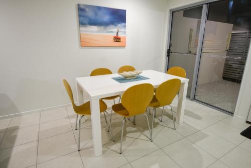 a dining room with a white table and yellow chairs at Direct Collective - Breeze on Brightwater in Mooloolaba