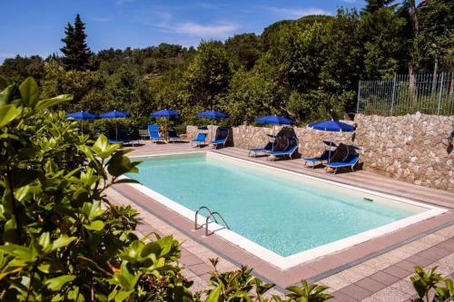 a swimming pool with chairs and blue umbrellas at Hotel Villa Paradiso in Riparbella