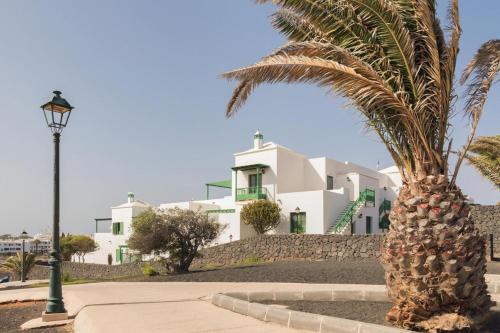 una palma di fronte a un edificio bianco di Apartamento OM con piscina y vistas al mar a Costa Teguise