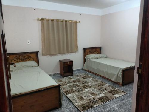 a bedroom with two beds and a table and a window at Dakrour flat in ‘Izbat Ţanāţī