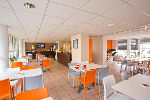 a restaurant with white tables and orange chairs at All Suites Appart Hôtel - Bordeaux - Mérignac Aéroport in Mérignac