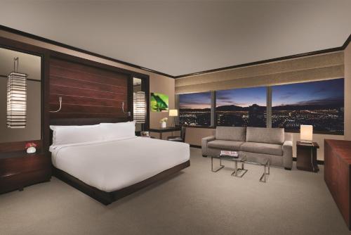 a bedroom with a bed and a couch and windows at Gorgeous Suite Vdara 22nd FLR - POOL View - FREE Valet in Las Vegas