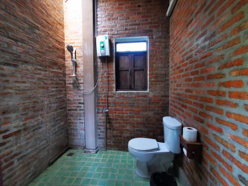 a bathroom with a toilet and a brick wall at Jasmine Hills Lodge in Doi Saket