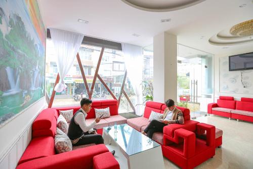 three people sitting in a living room with red couches at TTR Vincent Hotel in Da Lat