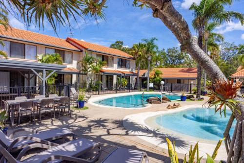 a resort pool with tables and chairs and palm trees at Wolngarin Holiday Resort Noosa in Noosaville