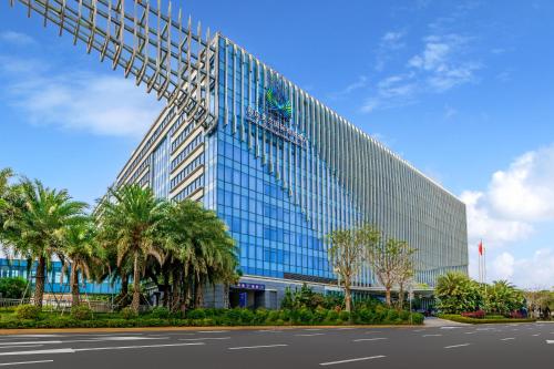 a tall glass building with palm trees in front of it at Haikou Meilan International Airport Hotel in Haikou