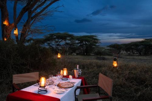 a dinner table with candles on a field at night at Serengeti Woodlands Camp in Serengeti