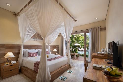 a bedroom with a bed and a desk and a television at Kailash Suites by Pramana Villas in Ubud