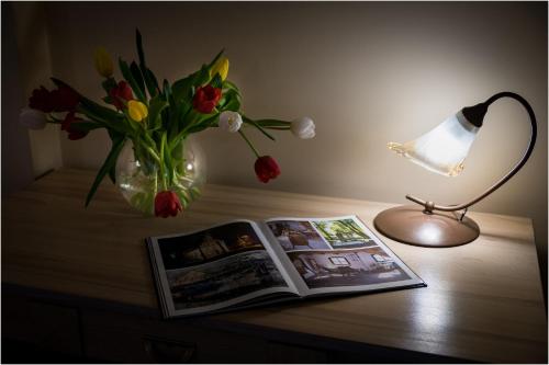 a table with a vase of flowers and a lamp and a book at Willa Centrum in Supraśl
