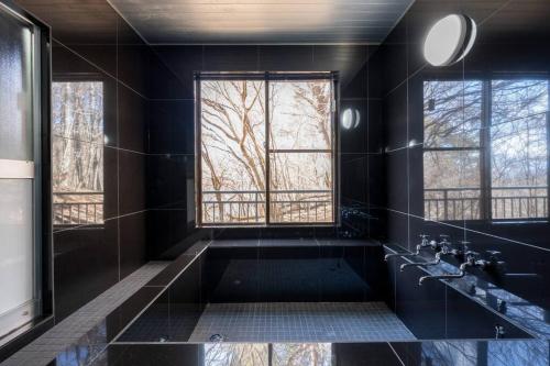 tj resort YAMANAKAKO Luxury large villa with Mt. Fuji, Sauna BBQ Max 25 في ياماناكاكو: حمام أسود مع حوض استحمام ونافذة