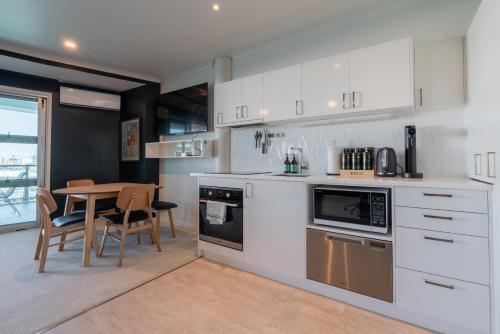 a kitchen with white cabinets and a table with chairs at Luxury Apartment - Parking - Hot Tub - Stunning Views in Auckland
