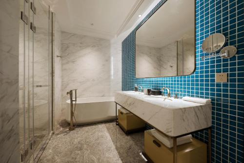 ein Badezimmer mit einem Waschbecken, einem Spiegel und einer Badewanne in der Unterkunft Qingdao Oriental Studio Chuangzhi SSAW Hotel in Qingdao