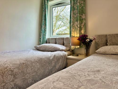 dwa łóżka w pokoju z oknem i wazonem kwiatów w obiekcie Relaxing 2 Bedroom Garden Cottage w mieście Coleraine