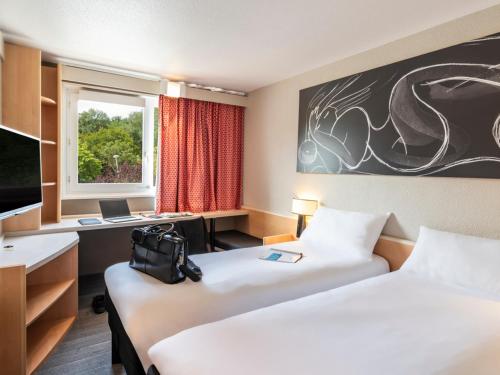 a hotel room with two beds and a desk at Ibis Paris Nord Villepinte Parc des Expositions in Roissy-en-France