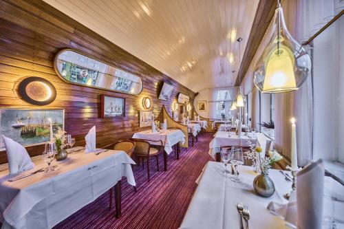 un restaurante con mesas y sillas blancas en una habitación en Janssens Hotel en Neuharlingersiel